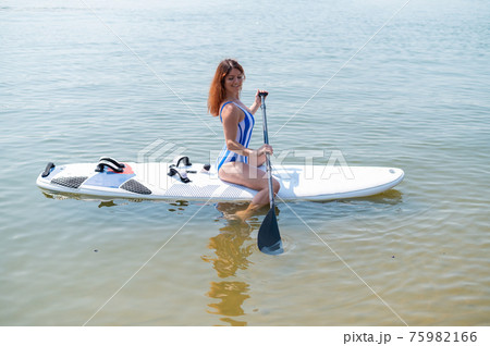 A woman in a swimsuit is posing lying on a sup board on the beach. 75982166