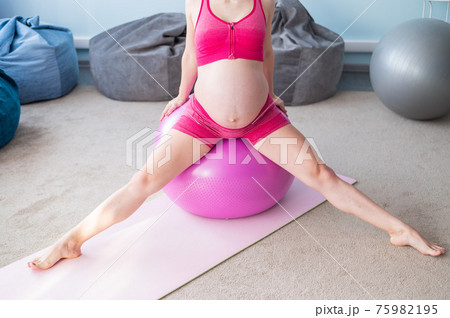 Cropped view of unrecognizable pregnant woman in yoga class. Future mother faceless with a bare tummy is engaged in fitness with a ball. Cropped view of unrecognizable pregnant woman in yoga class. Future mother faceless with a bare tummy is engaged in fitness with a ball. 75982195