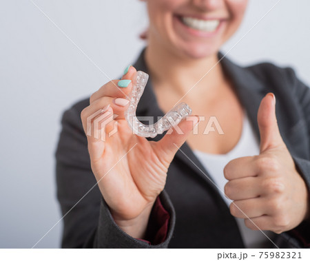 A woman in a jacket shows her thumbs up and demonstrates mouth guards to align the bite. The girl approves of the plastic removable braces for the teeth 75982321