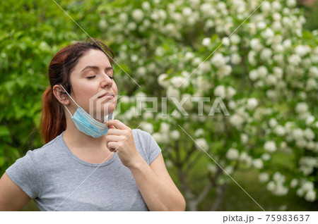 Happy woman pulls down a mask outdoors. A joyful girl walks in the park alone and takes off a medical mask. Social distance. Coronavirus is over. 75983637