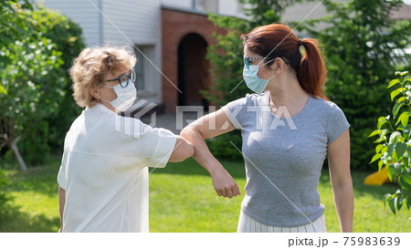 Women in medical masks greet their elbows outside. An elderly woman and her adult daughter maintain a social distance in the park during the coronavirus epidemic. New handshake bumping elbows 75983639