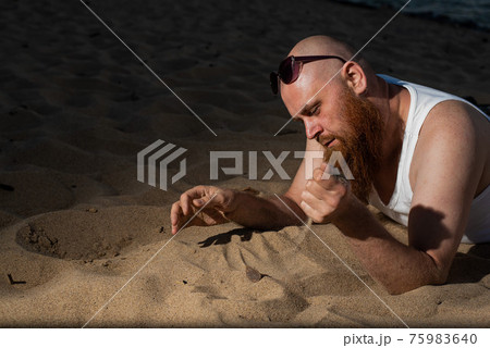A humorous portrait of a brutal man in a T-shirt and boxers on the beach at sunset 75983640