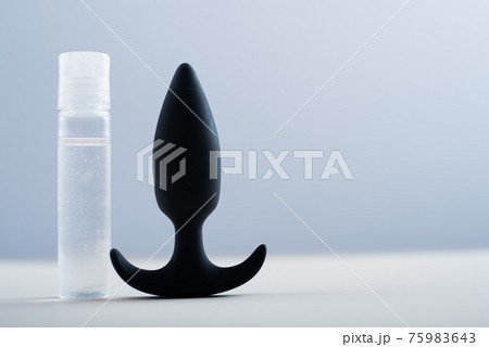 BLACK ANAL PLUG AND A BOTTLE OF LUBRICANTS ON A TABLE ON A WHITE BACKGROUND. 75983643