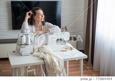 Young caucasian woman sews at home Young caucasian woman sews at home 75984464