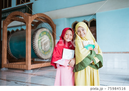 two smiling Muslim girls holding al quran book in their hands 75984516