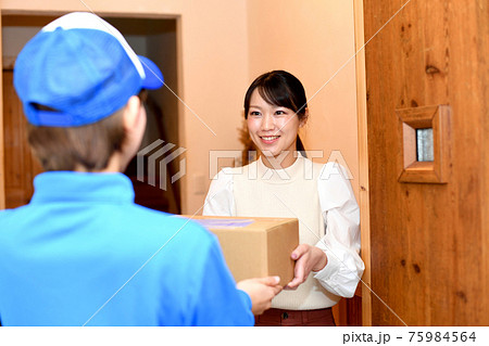 作業員から荷物（宅配便）を玄関で受け取る若い女性 75984564
