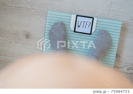 Top view on female legs in gray socks on electronic scales. Very heavy weight. The surprise of the increase in kg on a diet. The question is what the fuck? Fat woman with a big bare belly. 75984755