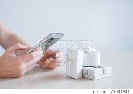 A faceless woman sits at a table and holds a mobile and a credit card in her hands. Online shopping for gifts concept 75984981