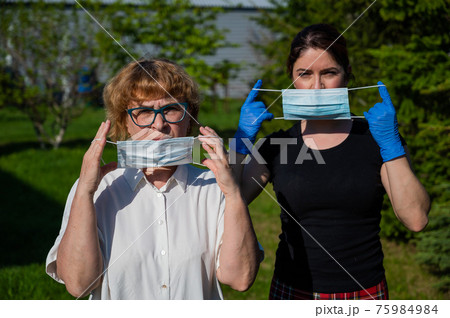 Mom and daughter put on medical masks against the spread of infection. Two elderly and middle-aged women are protected against coronavirus. 75984984