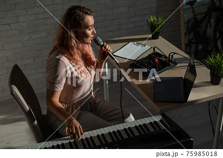 A female blogger sings and plays the live electronic piano. Portrait of a girl recording a song on a web camera and composing on a synthesizer. Online music lessons. Distance learning in quarantine. A female blogger sings and plays the live electronic piano. Portrait of a girl recording a song on a web camera and composing on a synthesizer. Online music lessons. Distance learning in quarantine. 75985018