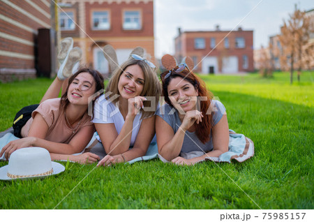 Three beautiful Caucasian young women lie on the lawn in the countryside. The blonde brunette and the redhead are resting in the park on the green grass. The friends had an outdoor picnic. Three beautiful Caucasian young women lie on the lawn in the countryside. The blonde brunette and the redhead are resting in the park on the green grass. The friends had an outdoor picnic. 75985157