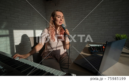 A female blogger sings and plays the live electronic piano. Portrait of a girl recording a song on a web camera and composing on a synthesizer. Online music lessons. Distance learning in quarantine. A female blogger sings and plays the live electronic piano. Portrait of a girl recording a song on a web camera and composing on a synthesizer. Online music lessons. Distance learning in quarantine. 75985199