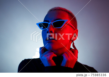Portrait of a young woman with a short male haircut in sunglasses in neon light in the studio 75985336