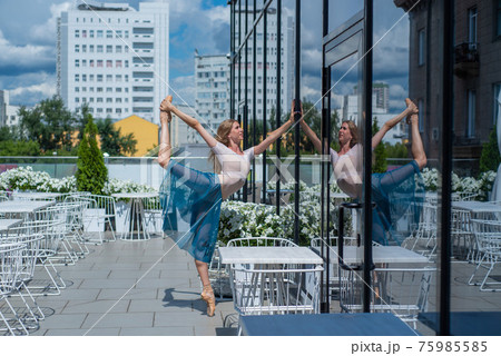 A beautiful ballerina is dancing outdoors on a warm summer day. Young flexible woman in pointe shoes and ballet tutu posing in a street cafe A beautiful ballerina is dancing outdoors on a warm summer day. Young flexible woman in pointe shoes and ballet tutu posing in a street cafe 75985585