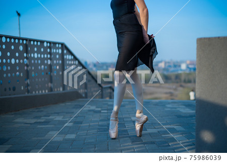Ballerina in ballet legs in shoes and black tutu dancing by the fence. Beautiful young woman in black dress and pointe dancing outside. Gorgeous ballerina performing a dance outdoors. Close up Ballerina in ballet legs in shoes and black tutu dancing by the fence. Beautiful young woman in black dress and pointe dancing outside. Gorgeous ballerina performing a dance outdoors. Close up 75986039