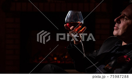 Man drinking whiskey by the fireplace. Man drinking whiskey by the fireplace. 75987288