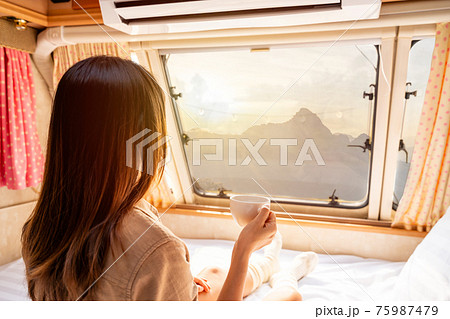 Young woman traveler with cup of coffee laying in camper van and looking beautiful landscape while road trip traveling on vacation 75987479