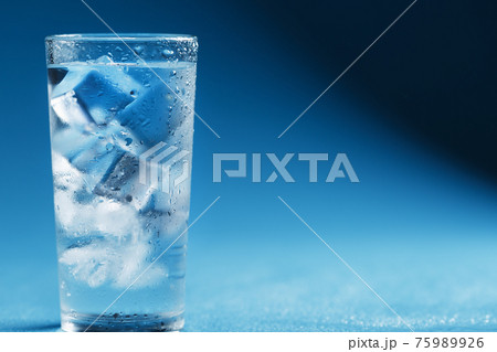 A glass with ice water and ice cubes on a blue background. 75989926
