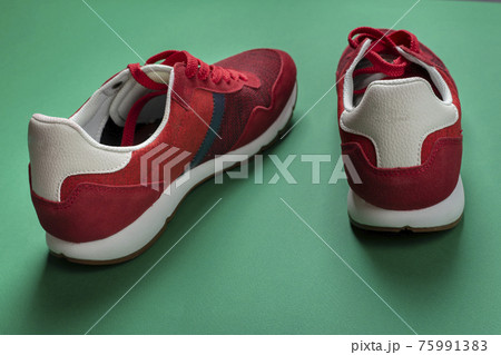 Pair of new red sneakers on a green background. Casual shoes. Space for text. 75991383