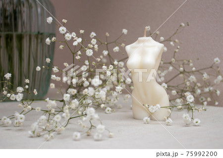 Candle figure of a woman on a table with a vase of white flowers Candle figure of a woman on a table with a vase of white flowers 75992200