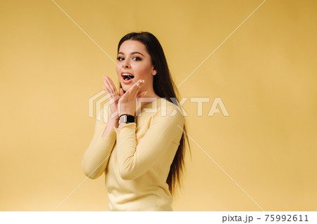 Happy surprised woman in yellow sweatshirt posing to photographer. Portrait of pretty woman on gray background Happy surprised woman in yellow sweatshirt posing to photographer. Portrait of pretty woman on gray background 75992611