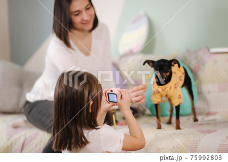 Young daughter photographer make photo of her mom play with dog at home. Toy camera for kids Young daughter photographer make photo of her mom play with dog at home. Toy camera for kids 75992803