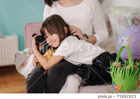 Little daughter with mom play with dog at home. Happy family preparing for easter Little daughter with mom play with dog at home. Happy family preparing for easter 75992825