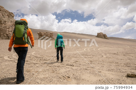 Two women hikers hiking on sand desert Two women hikers hiking on sand desert 75994934