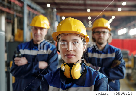 Young serious female worker of large industrial plant or factory in workwear and protective helmet 75996519