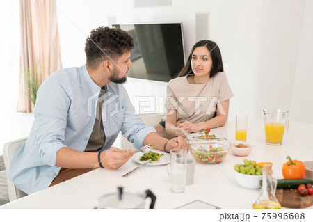 Young brunette woman looking at her husband during conversation by breakfast in the morning Young brunette woman looking at her husband during conversation by breakfast in the morning 75996608
