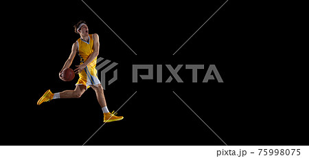 Young Caucasian basketball player training isolated on black background. Young Caucasian basketball player training isolated on black background. 75998075