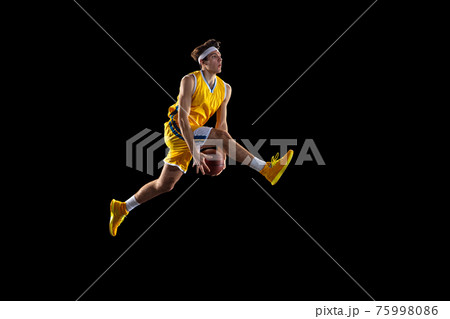 Young Caucasian basketball player training isolated on black background. Young Caucasian basketball player training isolated on black background. 75998086