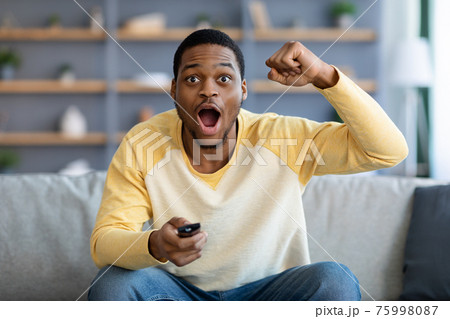 Emotional black man watching football game at home, copy space Emotional black man watching football game at home, copy space 75998087