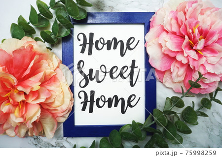 Home Sweet Home written on blue frame with green leave and pink flower flat lay on marble background 75998259