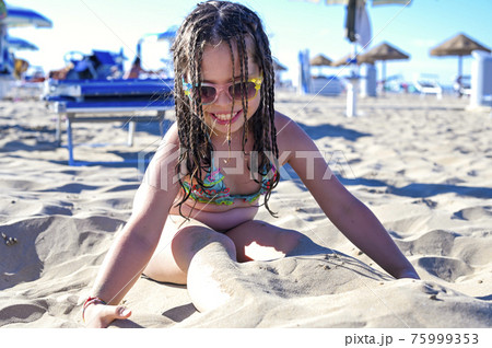 Little girl in a swimsuit on the beach plays, - Stock Photo [75999353] -  PIXTA