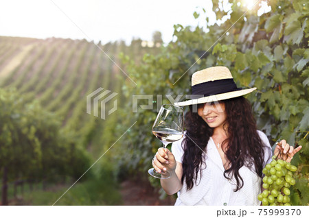 Young woman with a glass of white wine in the vineyards of Italy. Person pouring wine. Free space 75999370