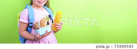 Young schoolgirl with lunch box on a green background. Little girl with a school backpack and a set 75999585