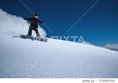 Young sportswoman woman on a snowboard rolls down a snowy slope against a blue sky on a sunny day 75999591