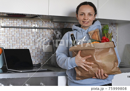 A person smiling for the camera with a set of food in hand.. Paper bag with Food supplies crisis A person smiling for the camera with a set of food in hand.. Paper bag with Food supplies crisis 75999808