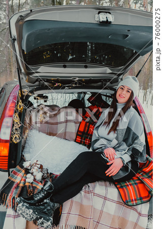 Brunette woman wrapped in blanket in trunk car. Travel in winter. Car decorated with festive Christmas lights. Outdoor picnic Brunette woman wrapped in blanket in trunk car. Travel in winter. Car decorated with festive Christmas lights. Outdoor picnic 76000275