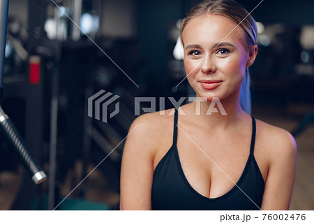 Close up portrait of a young blonde woman in sport bra in a dark gym Close up portrait of a young blonde woman in sport bra in a dark gym 76002476