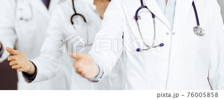 Group of doctors are standing as a team while offering their helping hands for shaking hand or saving people's life. Medicine concept during Coronavirus pandemic. Covid-2019 76005858