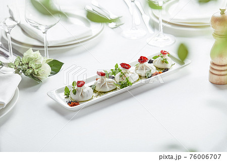 Fresh burata cheese with tomatoes and herbs on white plate 76006707