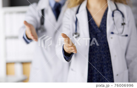Two doctors standing and offering helping hand for shaking hand or saving life. Medical help, countering viral infection and medicine concept 76006996