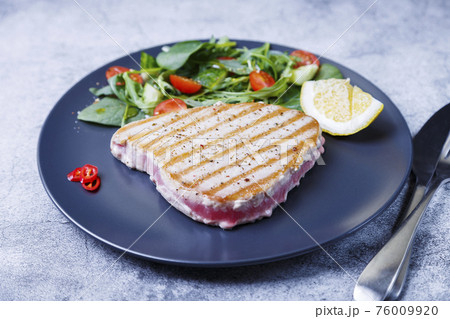 Grilled tuna steak with fresh vegetables, arugula, spinach and lemon. Close-up Grilled tuna steak with fresh vegetables, arugula, spinach and lemon. Close-up 76009920