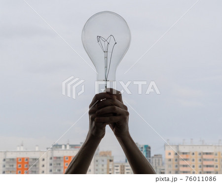 big electric light bulb in hands. incandescent lamp on the background of residential buildings. power supply big electric light bulb in hands. incandescent lamp on the background of residential buildings. power supply 76011086