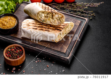Delicious fresh shawarma with meat and vegetables on a dark concrete table Delicious fresh shawarma with meat and vegetables on a dark concrete table 76011917