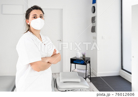 Confident female physiotherapist posing in modern clinic wearing protective face mask during Confident female physiotherapist posing in modern clinic wearing protective face mask during 76012606