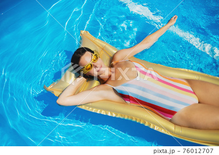 Top view of young woman in swimming pool outdoors on floating bed, relaxing. Top view of young woman in swimming pool outdoors on floating bed, relaxing. 76012707
