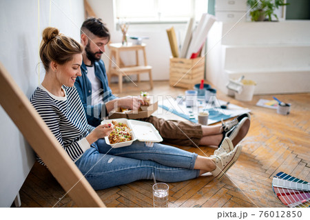Couple eating lunch indoors at home, relocation, diy and food delivery concept. Couple eating lunch indoors at home, relocation, diy and food delivery concept. 76012850